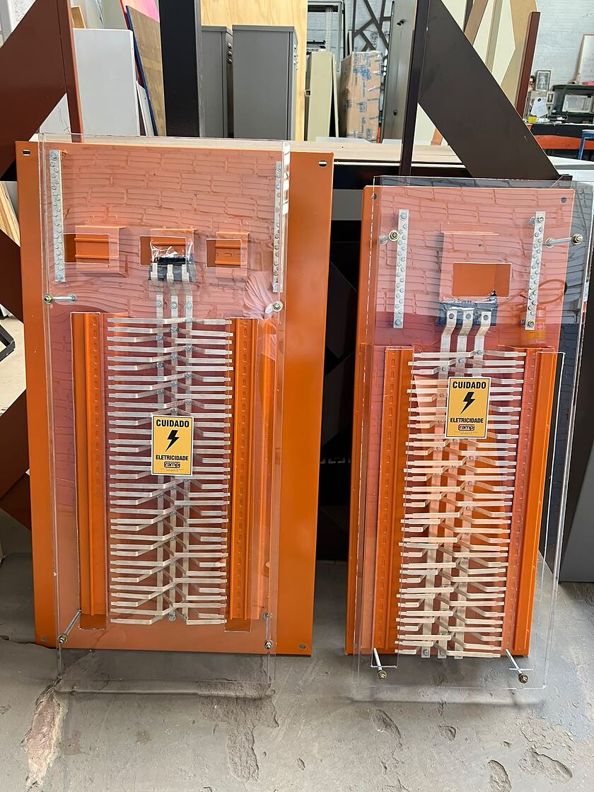 Dois painéis de barramentos elétricos com placas de fixação revestidas em tinta eletrostática a pó Laranja 2003 e proteção acrílica transparente